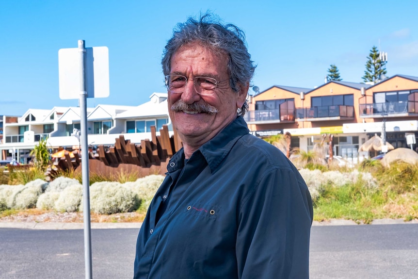 An old man standing outside with shops and accommodation in the background