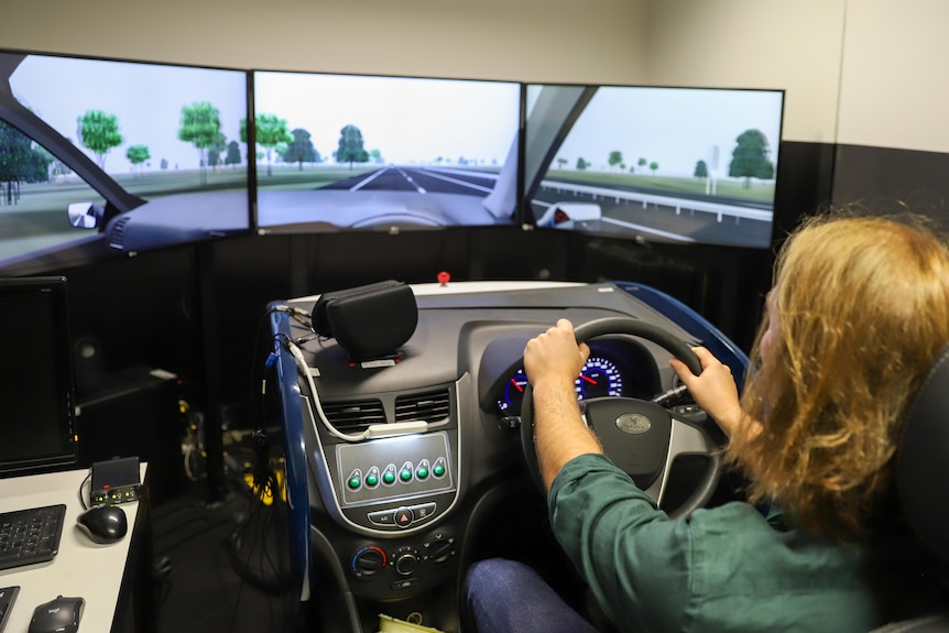 A man driving a virtual car on computer screens