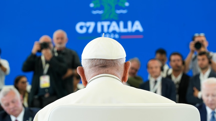 The pope sits with his back to the camera, with the words G7 Italia above him 