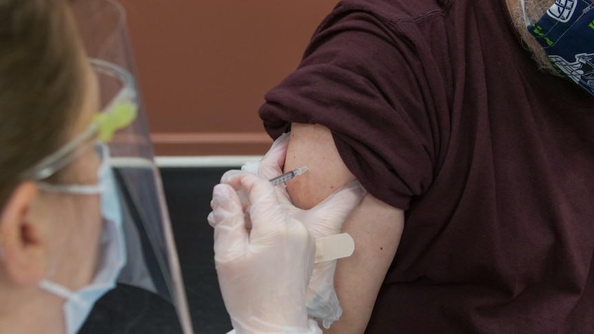 A nurse in mask and gloves prepares to put a needle in a man's arm 