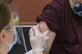 A nurse in mask and gloves prepares to put a needle in a man's arm 