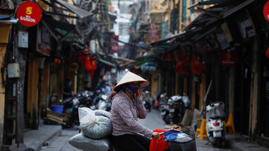 A woman on a bike wears a protective mask as she rides past an empty street in Hanoi