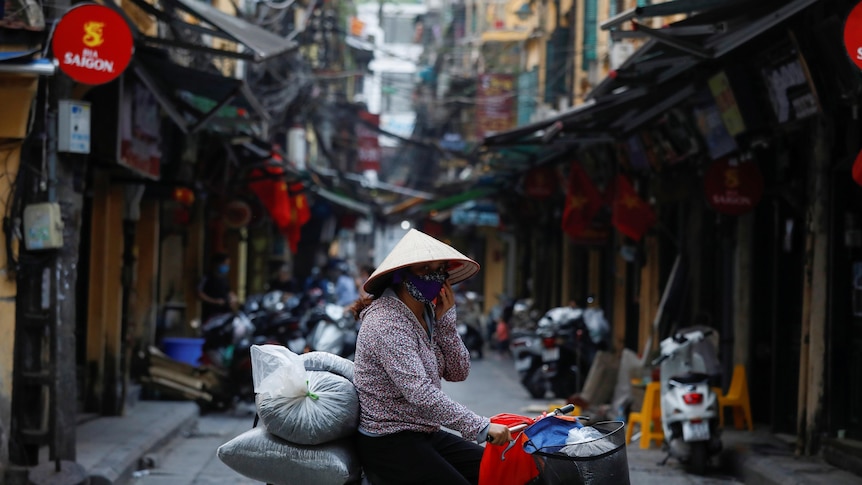 A woman on a bike wears a protective mask as she rides past an empty street in Hanoi