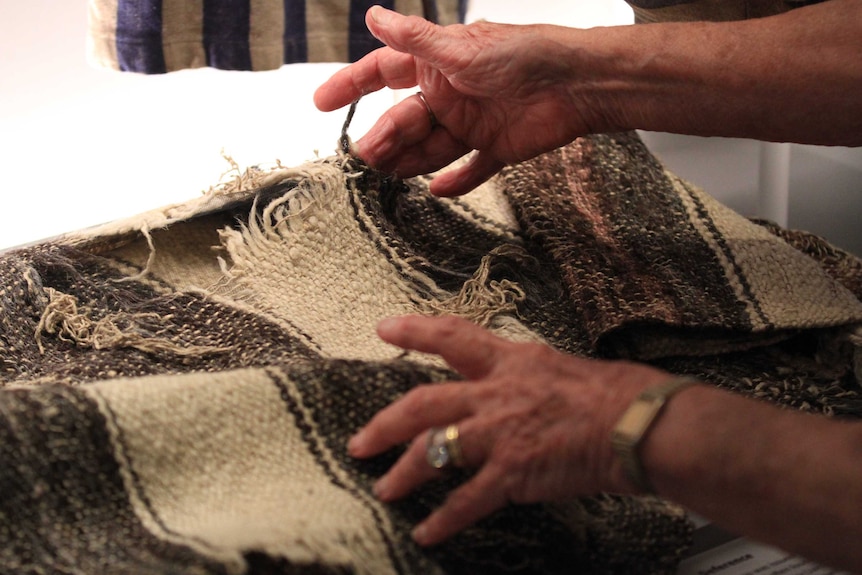 An older woman's hands can be seen gently touching a black and white woven blanket.