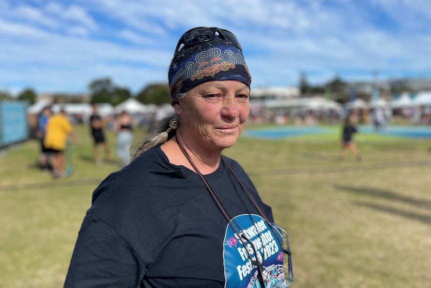 An Aboriginal woman with a headband and blue t-shirt on, standing on a field in the sunshine.