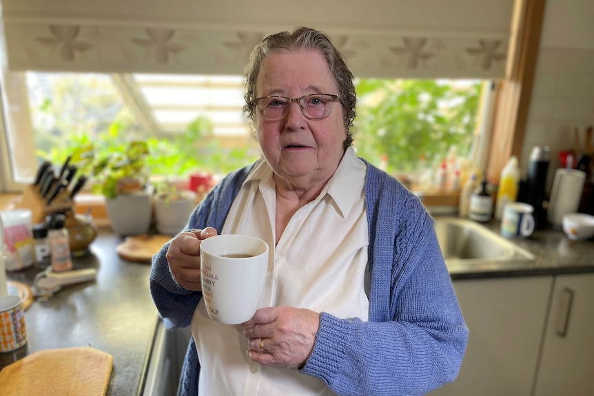 An elderly woman holds a cup of tea.