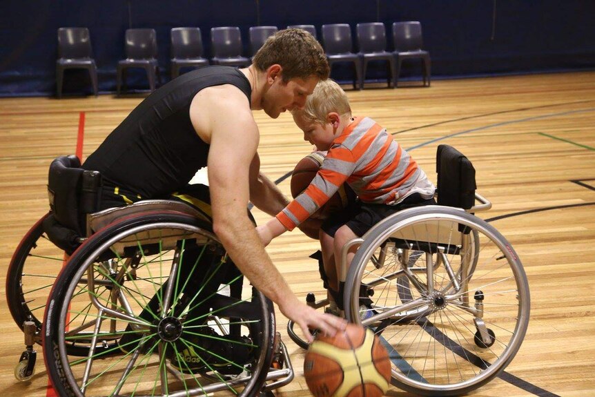 man and young boy both in wheelchairs each hold a basketball and are practising bouncing it.