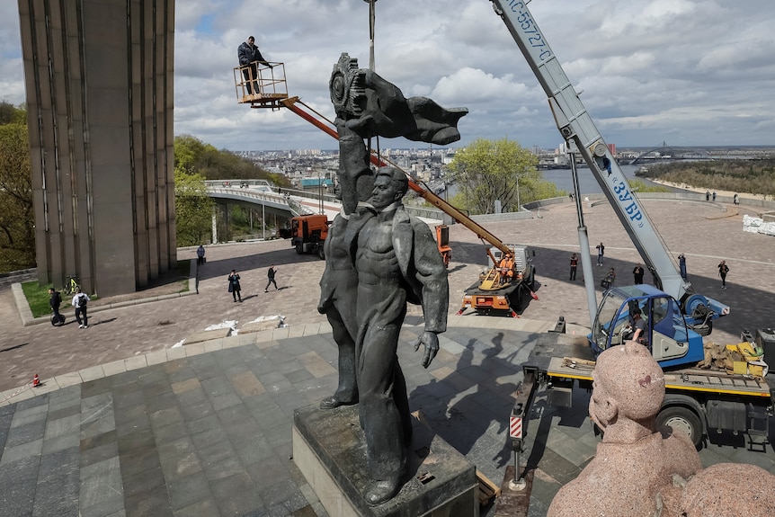 Una grúa desmantelando una estatua de bronce de un hombre.