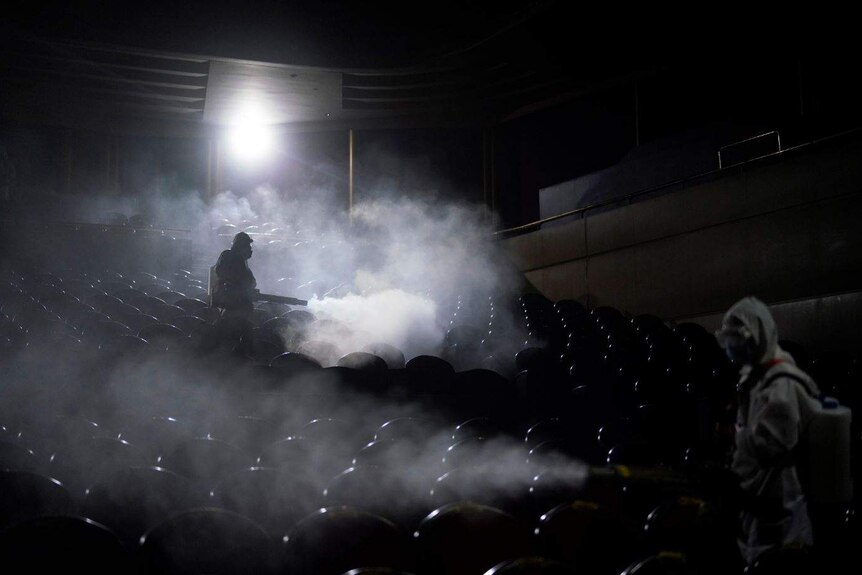 Men in hazmat gear spray gas around an empty theatre