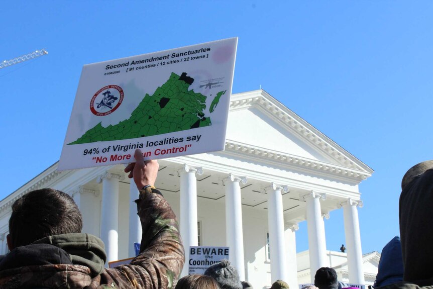 a man in a jacket holds up sign saying virginians do not want more gun control in a crowd outside the capitol building