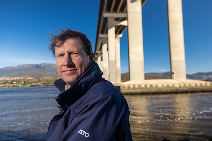 Craig Davey smiles at the camera with the Tasman Bridge behind him.