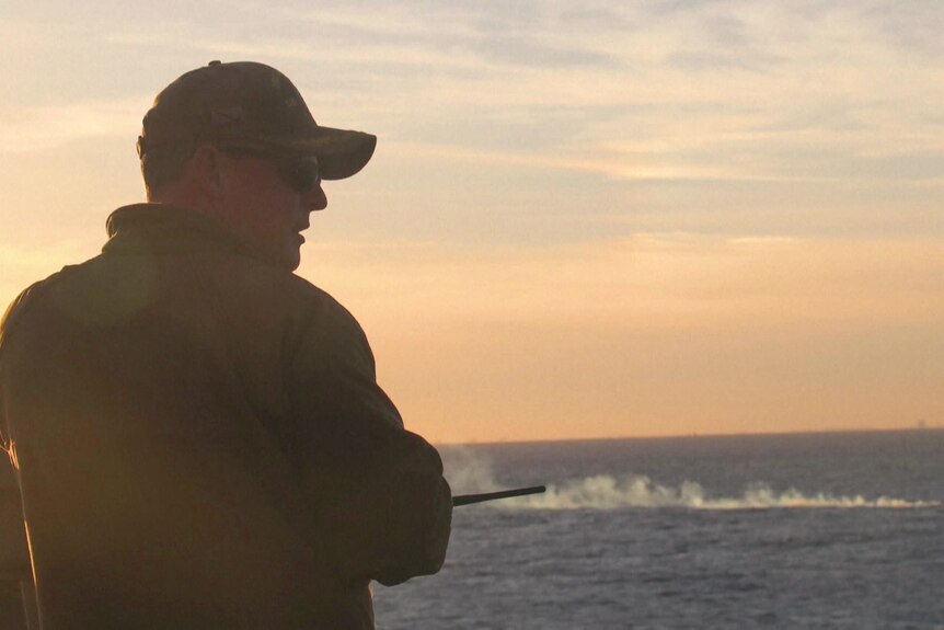 A person in military uniform looking over an ocean at dusk