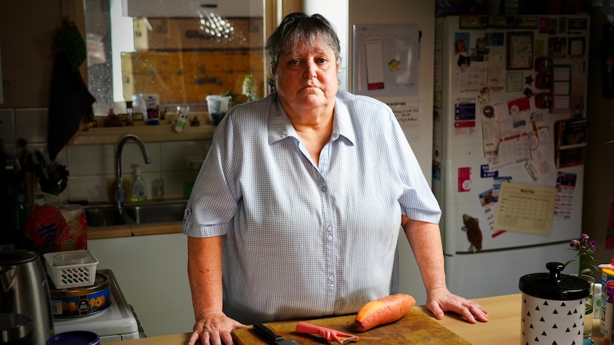 A woman standing at her kitchen bench with a sweet potato on a chopping board.