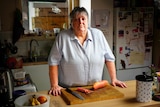 A woman standing at her kitchen bench with a sweet potato on a chopping board.