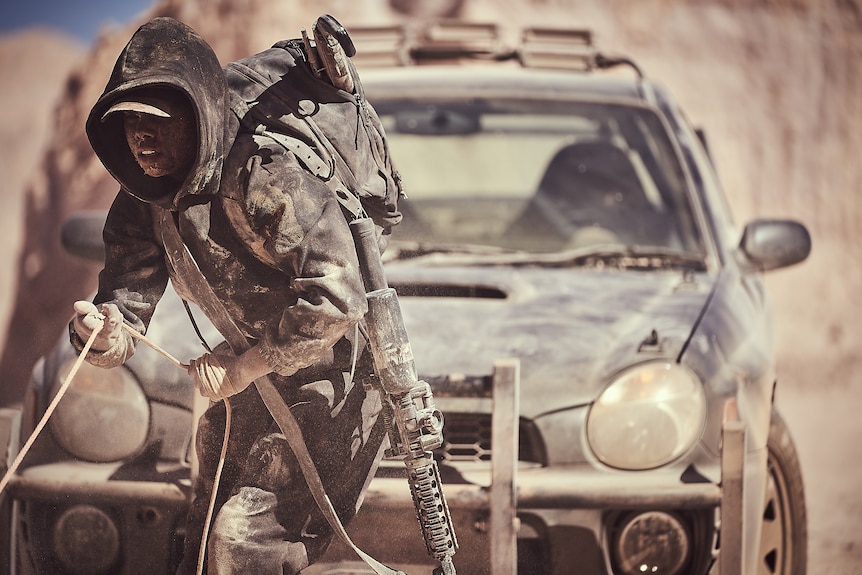 A woman wearing a hoody holds a rope and is covered in dust.