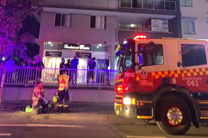 A fire engine and firefighters outside an apartment building at night. 