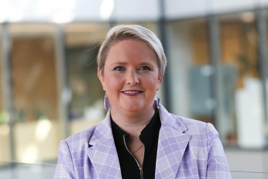 Verity porte un blazer violet et une chemise noire 