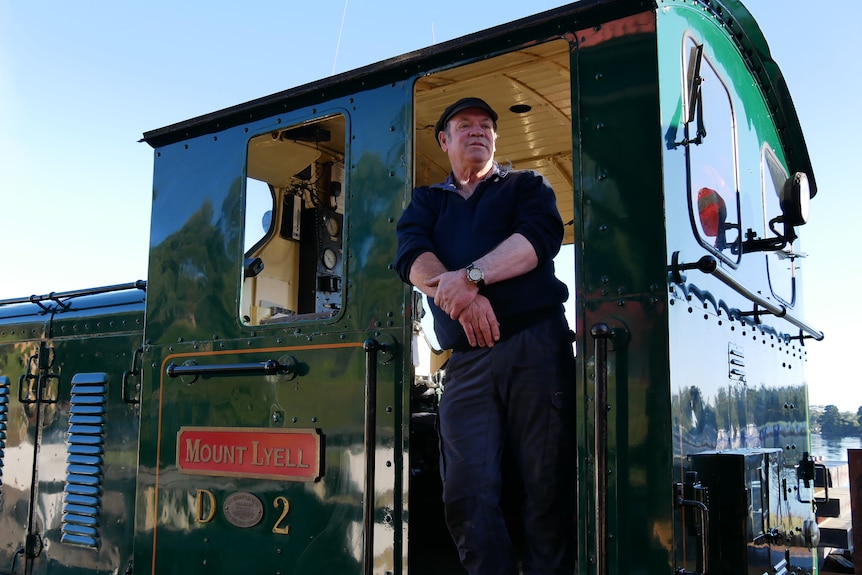 A train engine driver standing in doorway of green carriage.