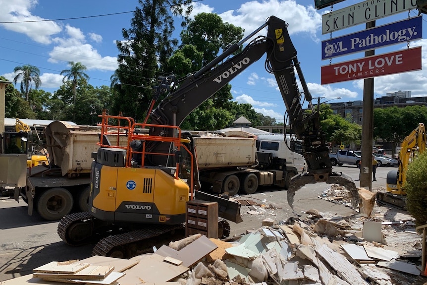 An excavator removes rubbish lying outside buildings on Molesworth St, Lismore.