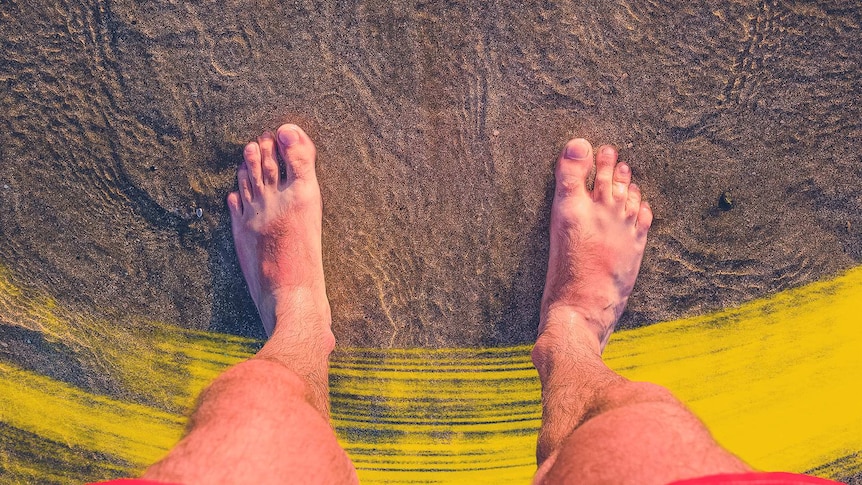 Top-down view of a man's feet on a beach in shallow ocean water which some say helps with wounds.