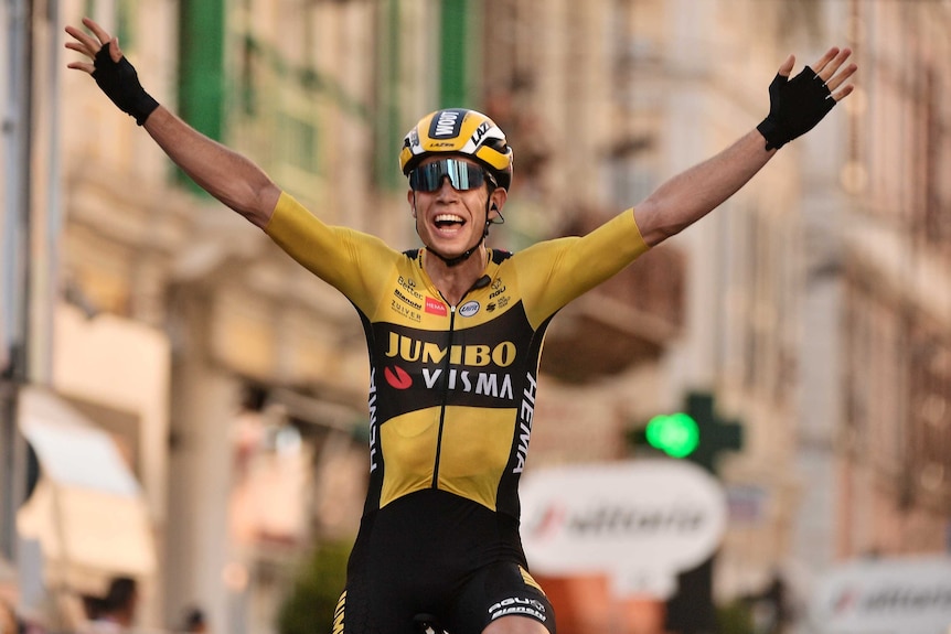 Wout van Aert smiles with his hands stretched in the air