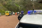 A police car and an officer parked in a nature park with an ambulance and emergency services in the distance