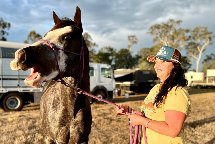 A paint breed of horse opens its mouth to whinny as a woman holds his lead and smiles.