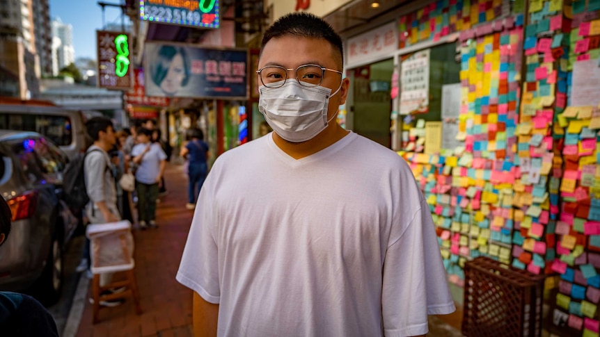 A man in a face mask standing in front of a restaurant covered in sticky notes