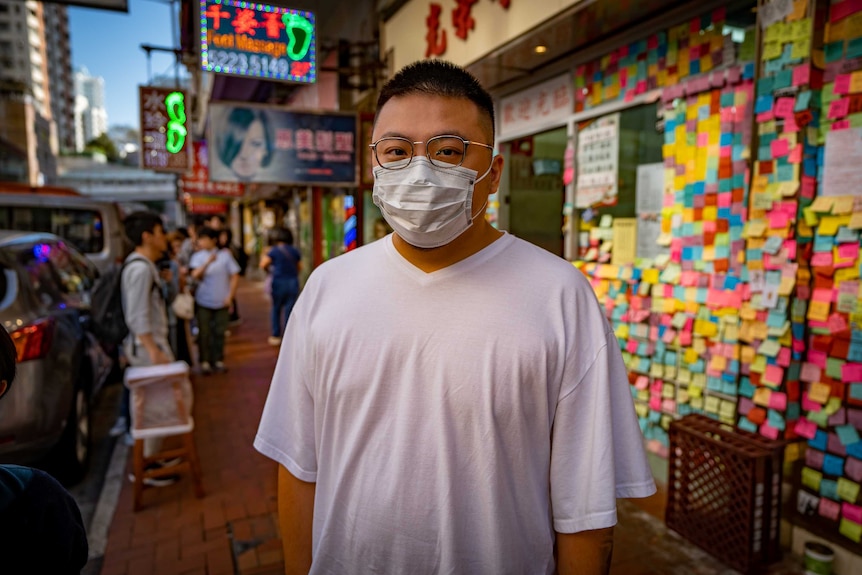 A man in a face mask standing in front of a restaurant covered in sticky notes