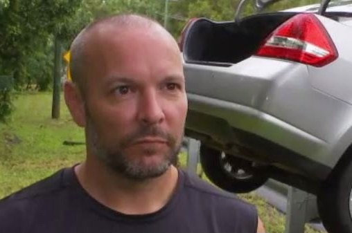 A man stands in front of a car on a guard rail.