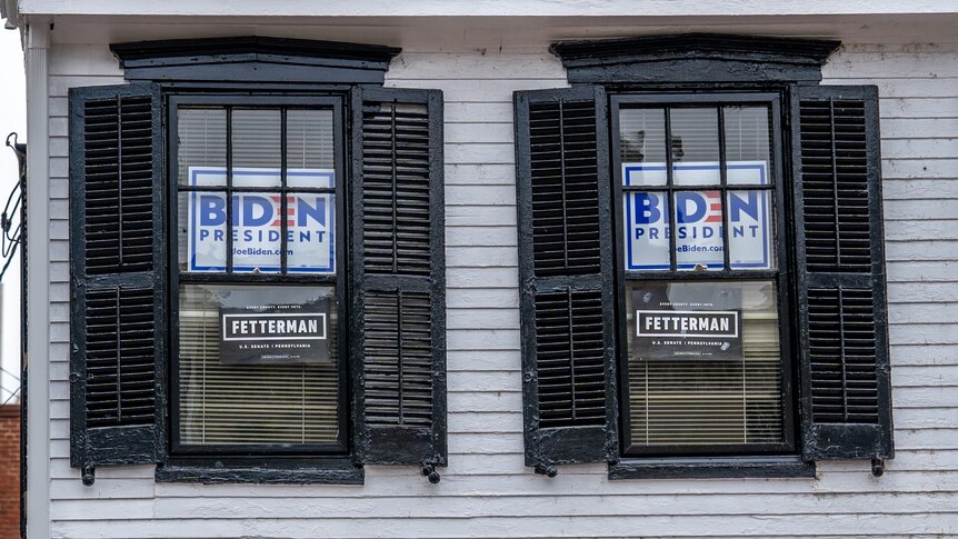 Two black-shuttered windows on a weatherboard house with signs that read "Biden for President"