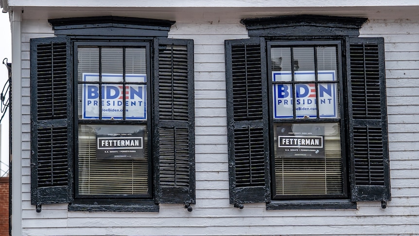 Two black-shuttered windows on a weatherboard house with signs that read "Biden for President"