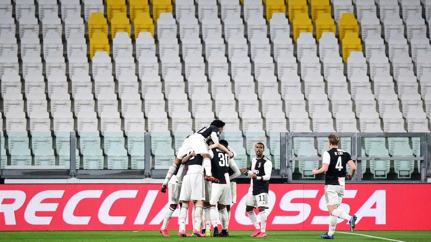 A huddle of players in black and white shirts celebrate in a soccer match in front of empty seats.