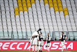 A huddle of players in black and white shirts celebrate in a soccer match in front of empty seats.