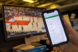 A man's hand holding a phone with betting odds. The phone is receiving a message from a group chat. 