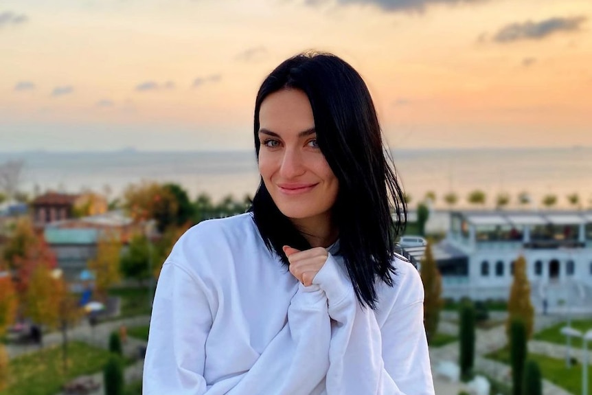 A young brunette woman stands on a balcony at sunset 