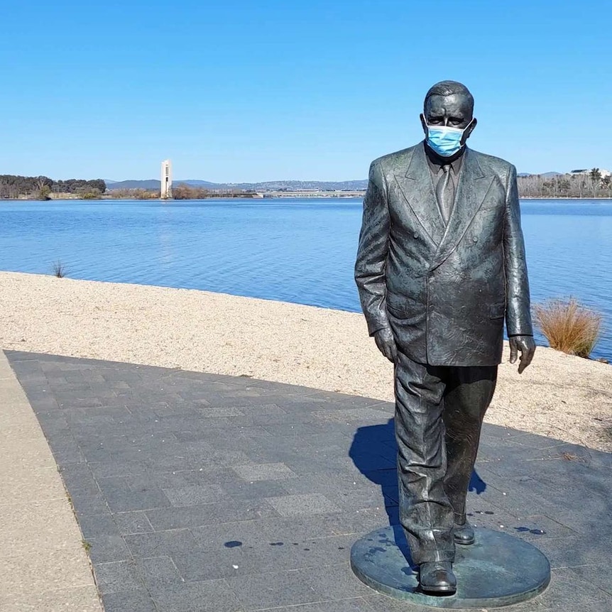 A statue of Robert Menzies, with a disposable mask on his face,