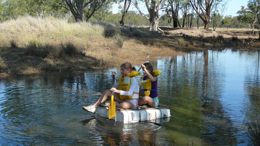 Marianne Haines and her twin sister paddling on a homemade raft made of chemical drums.
