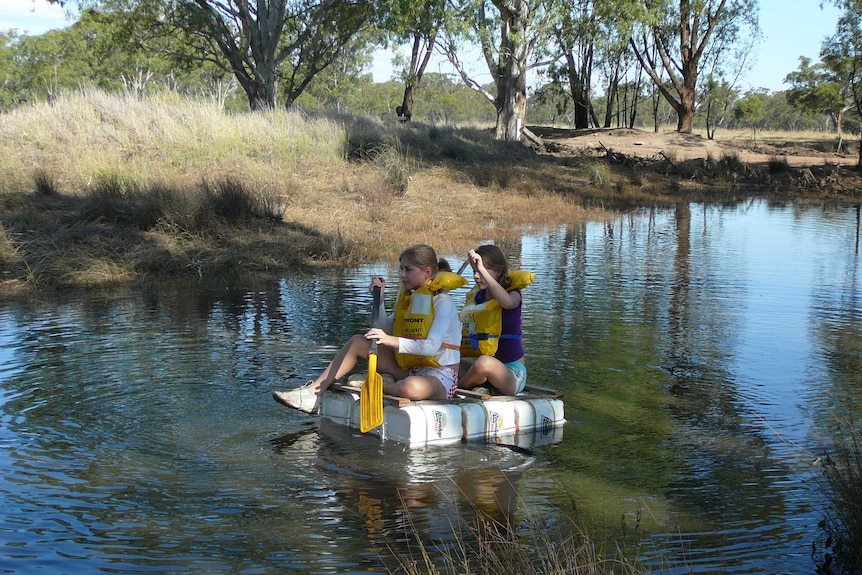 Marianne Haines and her twin sister paddling on a homemade raft made of chemical drums.