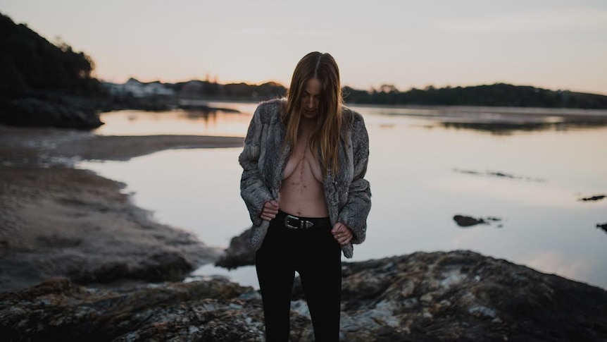 Young woman at the beach with furry coat on and large scar down chest