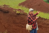 man stands in soil pit watched by crowd