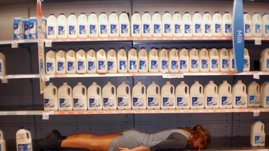 A woman planking in the milk section of a supermarket