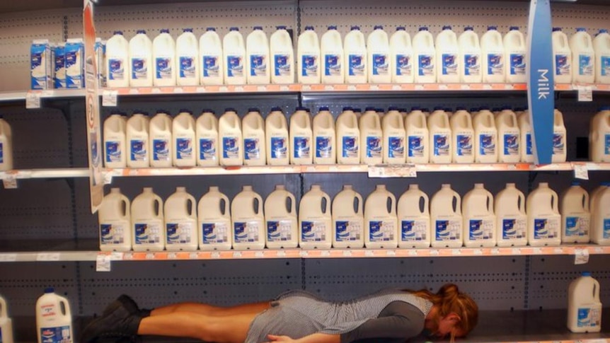 A woman planking in the milk section of a supermarket