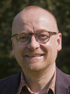A man wearing glasses smiles at the camera.