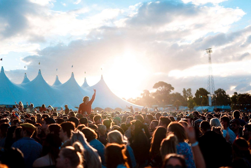 A crowd at Groovin' the Moo music festival where one woman is one another person's shoulders with her arm raised.