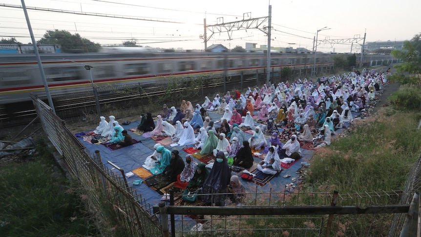 Hundreds of women pray during Eid as a metro train passes by