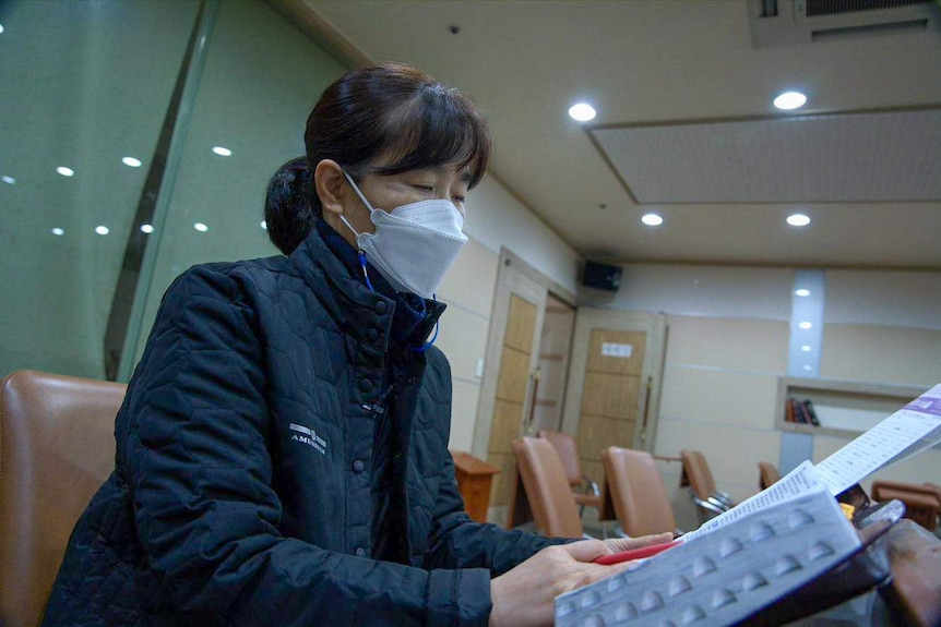 A Korean woman in a face mask looks at paper work