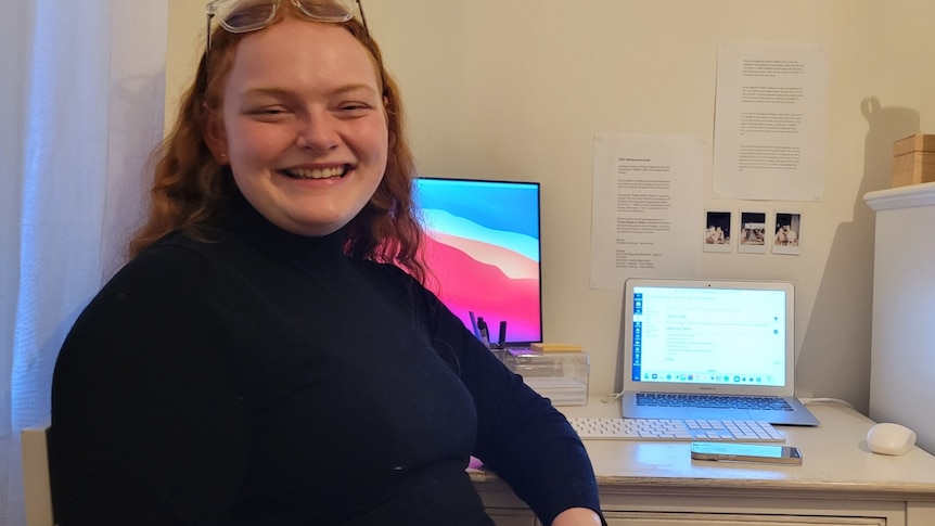 A young woman smiling next to a computer screen