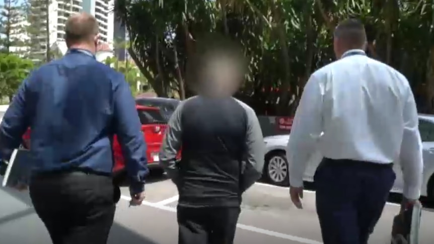 A man being led to a car by policemen.