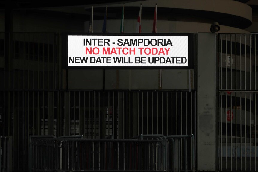 A white sign with red and black writing is attached to a darkened concrete stadium.